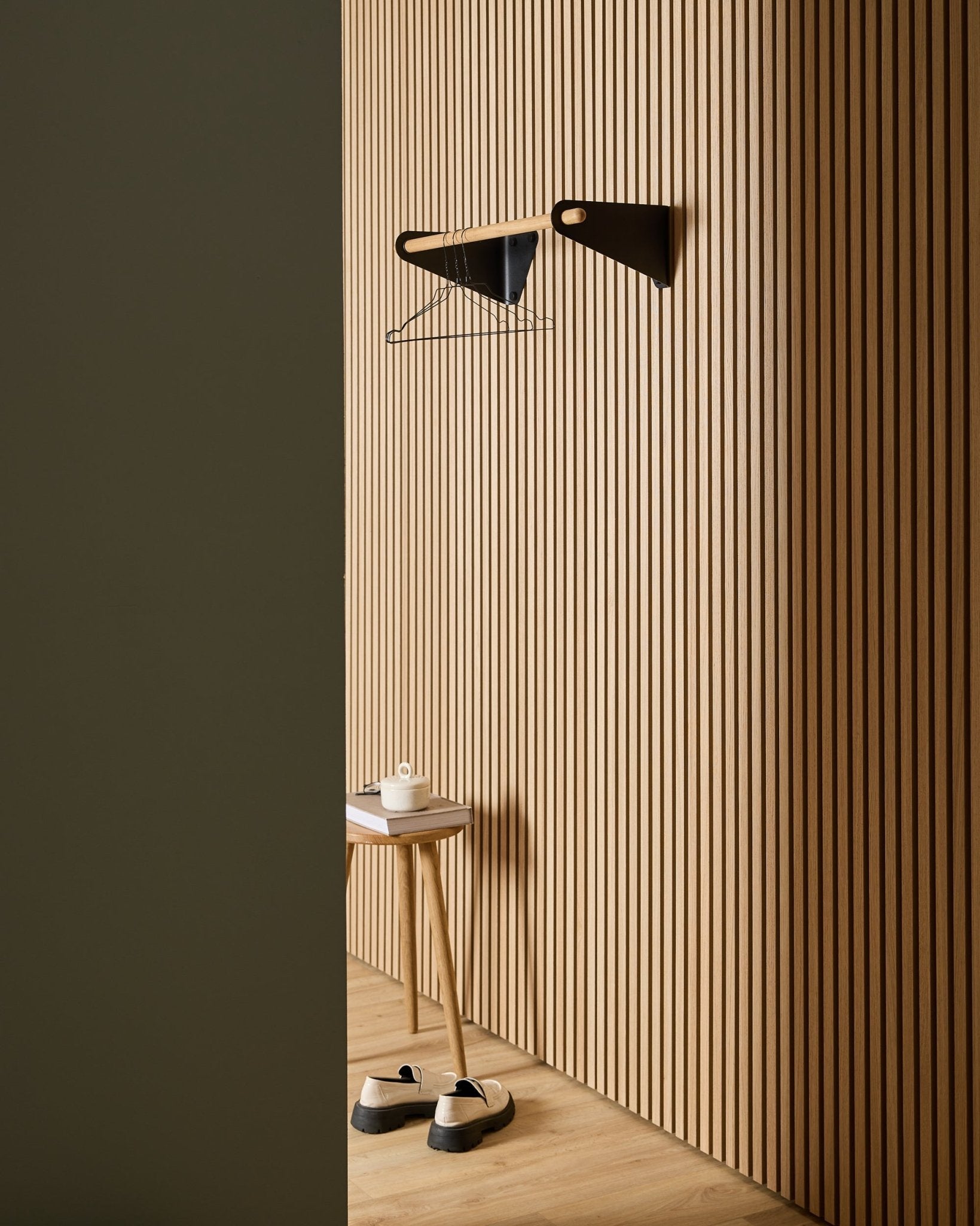 Minimalist entryway featuring WoodUpp Akupanel Nordic acoustic wood slatwall panels, black Linn Coat Rail (75.9 cm), stool, shoes, wall shelf, and paper roll.
